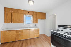 Kitchen with range with gas cooktop, light countertops, arched walkways, light wood finished floors, and wood finish cabinets
