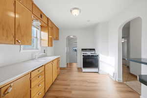Kitchen with arched walkways, light countertops, white gas range, and light wood-style flooring