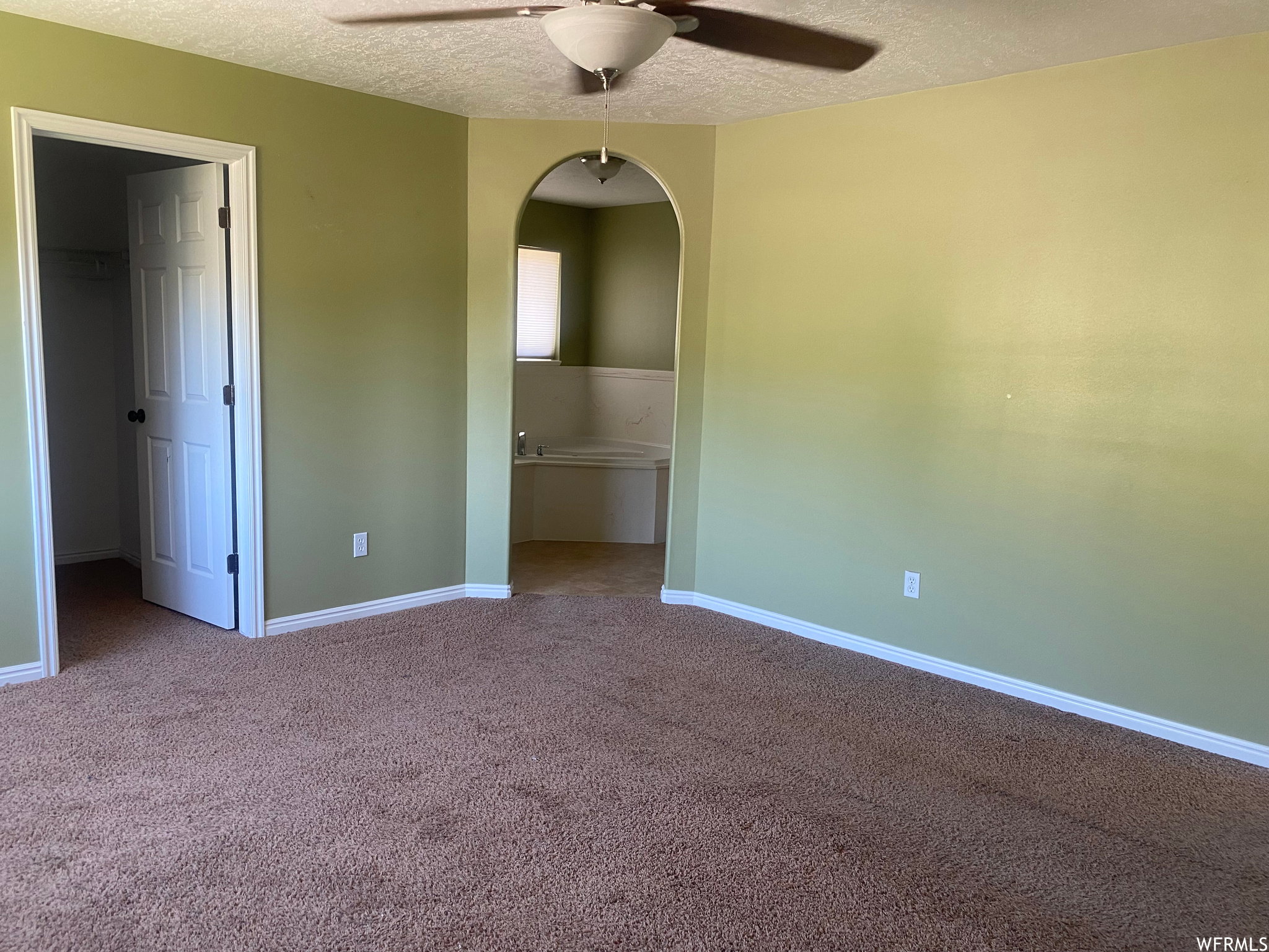 Unfurnished bedroom featuring arched walkways, carpet flooring, a walk in closet, a textured ceiling, and ceiling fan