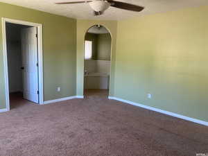 Unfurnished bedroom featuring arched walkways, carpet flooring, a walk in closet, a textured ceiling, and ceiling fan
