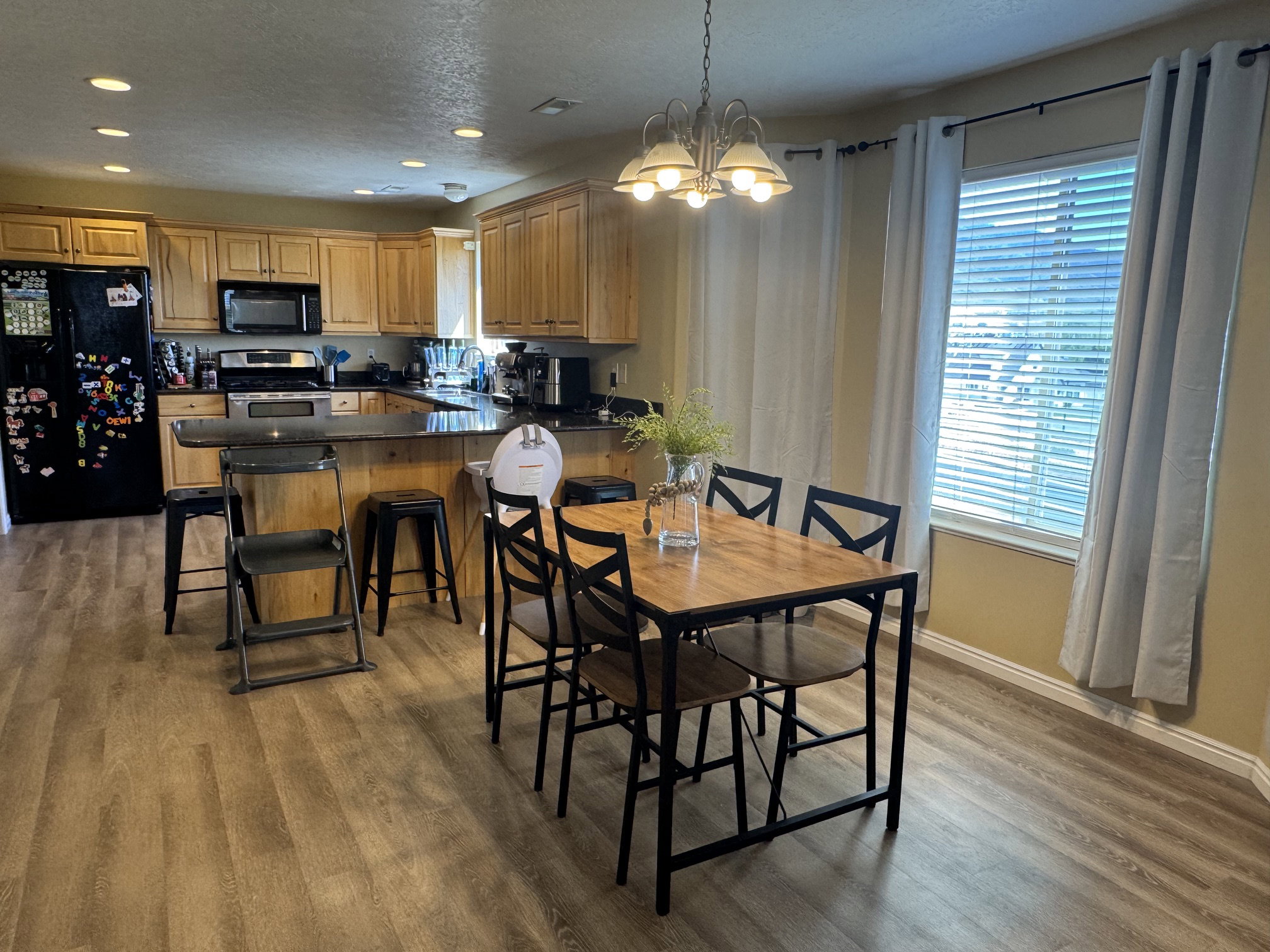 Open-concept kitchen and dining area featuring wood-finish flooring, recessed lighting, natural wood cabinetry, and a black appliance package