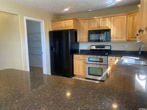Kitchen featuring black appliances, dark stone counters, light wood finish cabinets, recessed lighting, and a textured ceiling