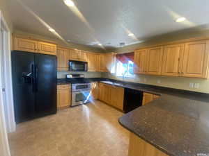 Kitchen with black appliances, dark stone countertops, light floors, and recessed lighting