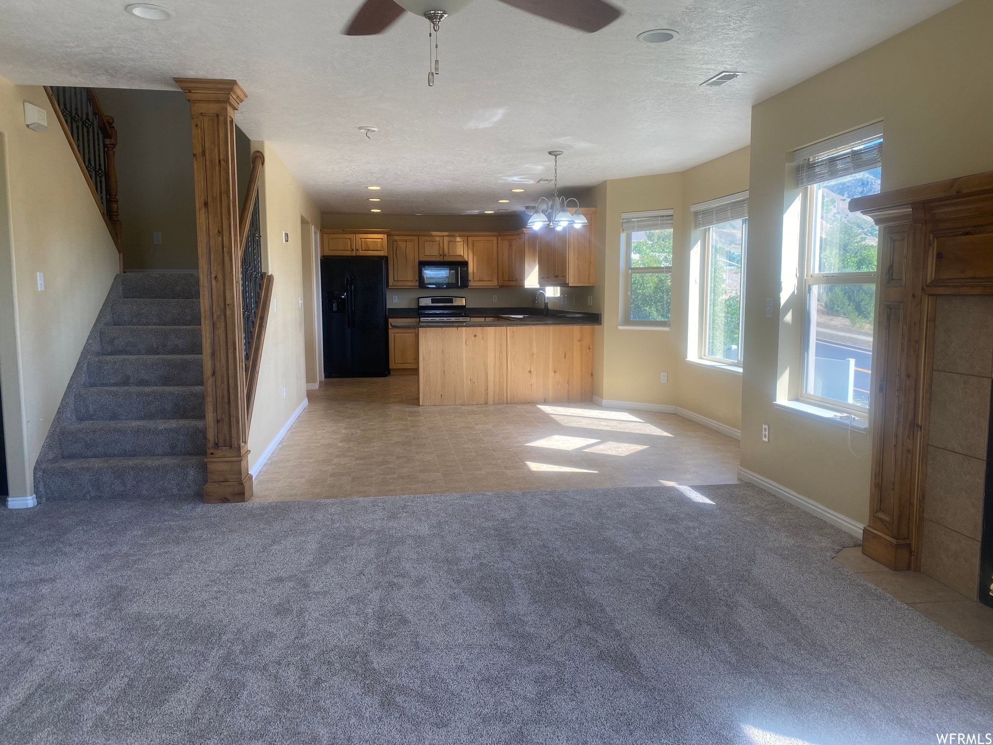 Kitchen with open floor plan, black appliances, dark countertops, light carpet, and a ceiling fan