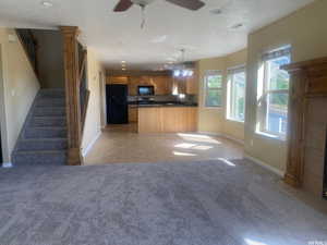 Kitchen with open floor plan, black appliances, dark countertops, light carpet, and a ceiling fan