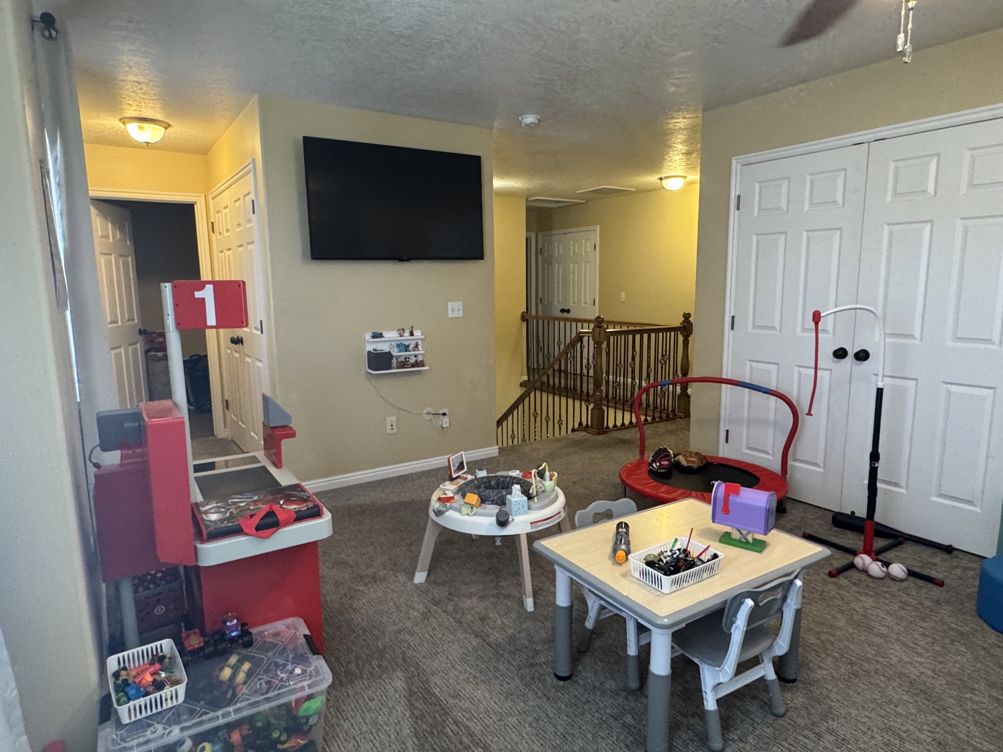 Carpeted bonus room featuring a wall-mounted television, a built-in closet with double bifold doors, and a wood-finish staircase with balusters