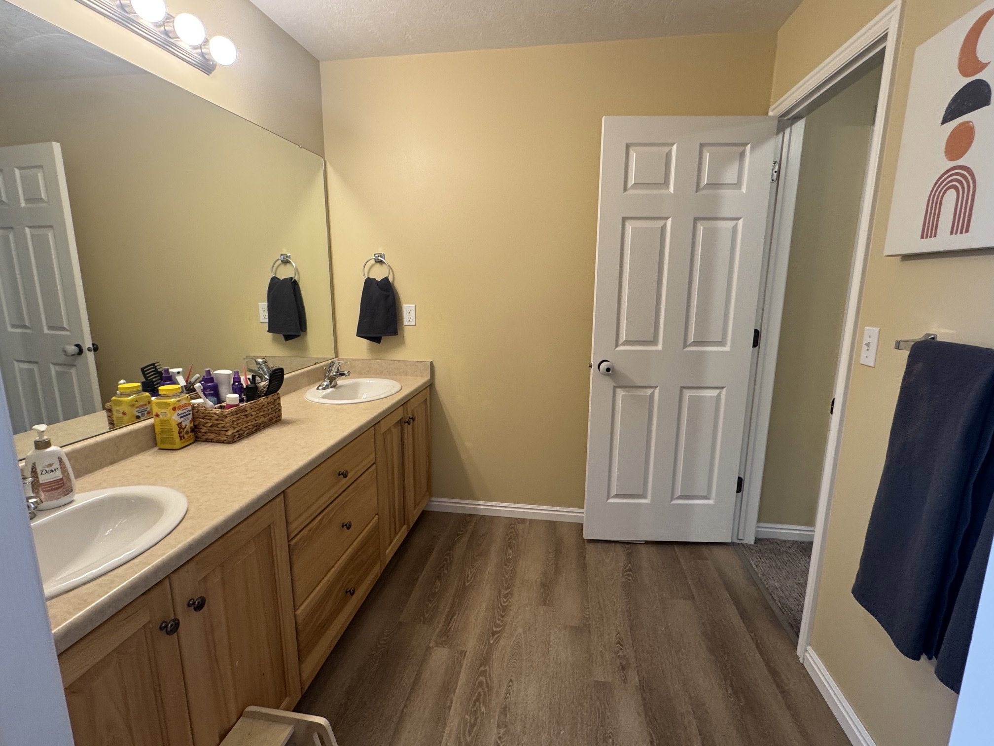 Spacious bathroom featuring a dual vanity with light wood cabinetry, white sinks, and a large wall-mounted mirror