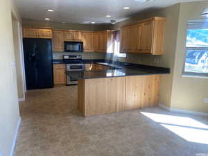 Kitchen featuring black appliances, a peninsula, dark stone counters, recessed lighting, and wood finish cabinetry