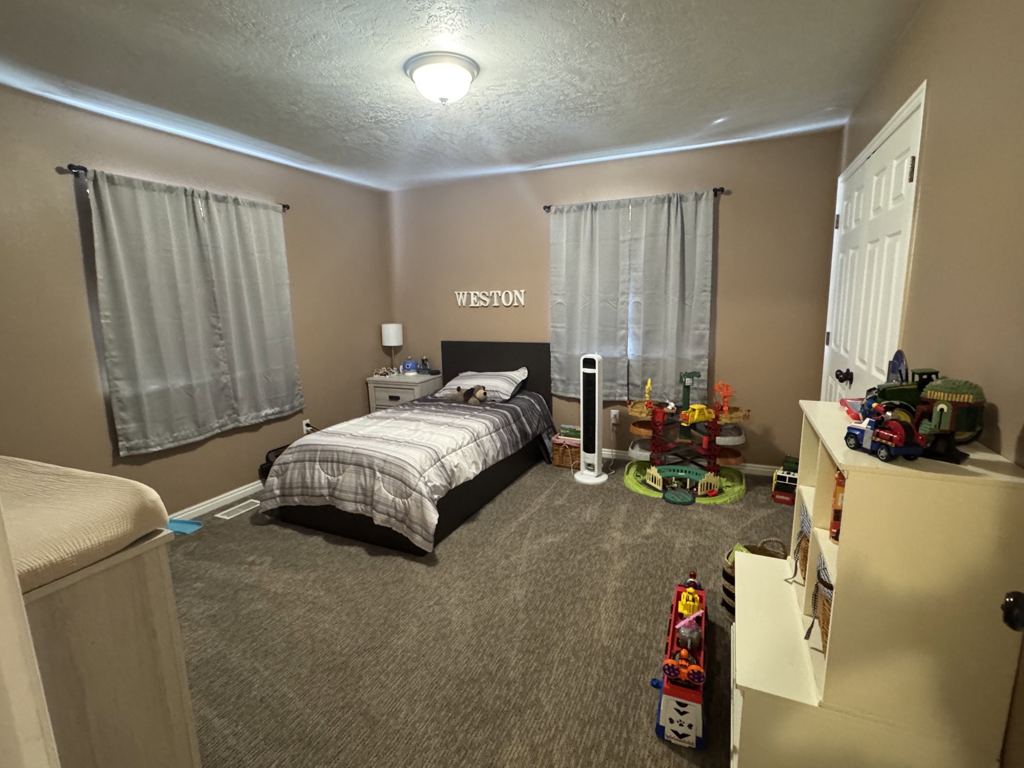 Bedroom featuring neutral-toned walls, textured ceiling, a flush-mount ceiling light fixture, and window with gray drapery