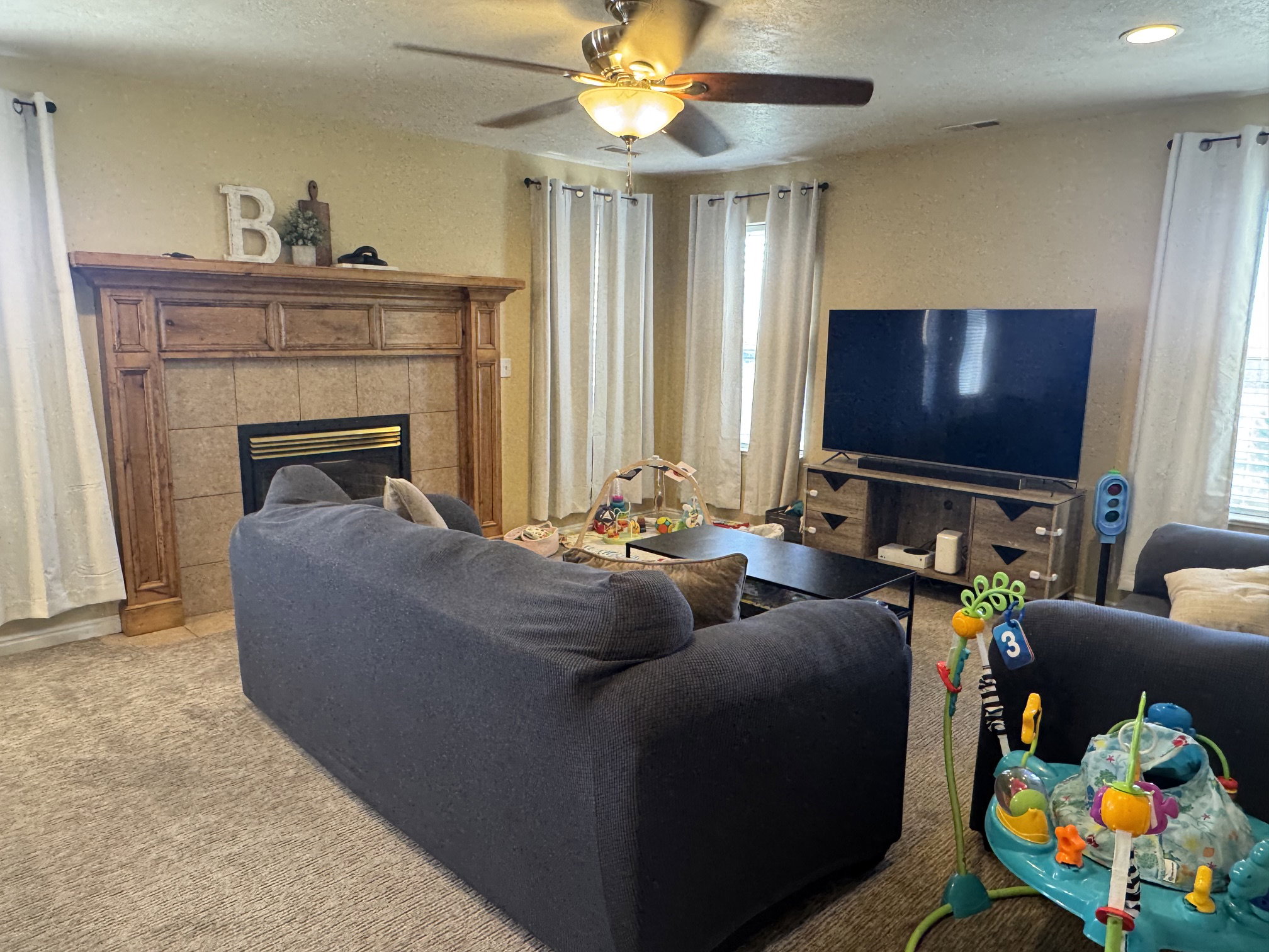 Living area featuring a fireplace with a wood mantle and tile surround, ceiling fan with integrated lighting, and carpet flooring
