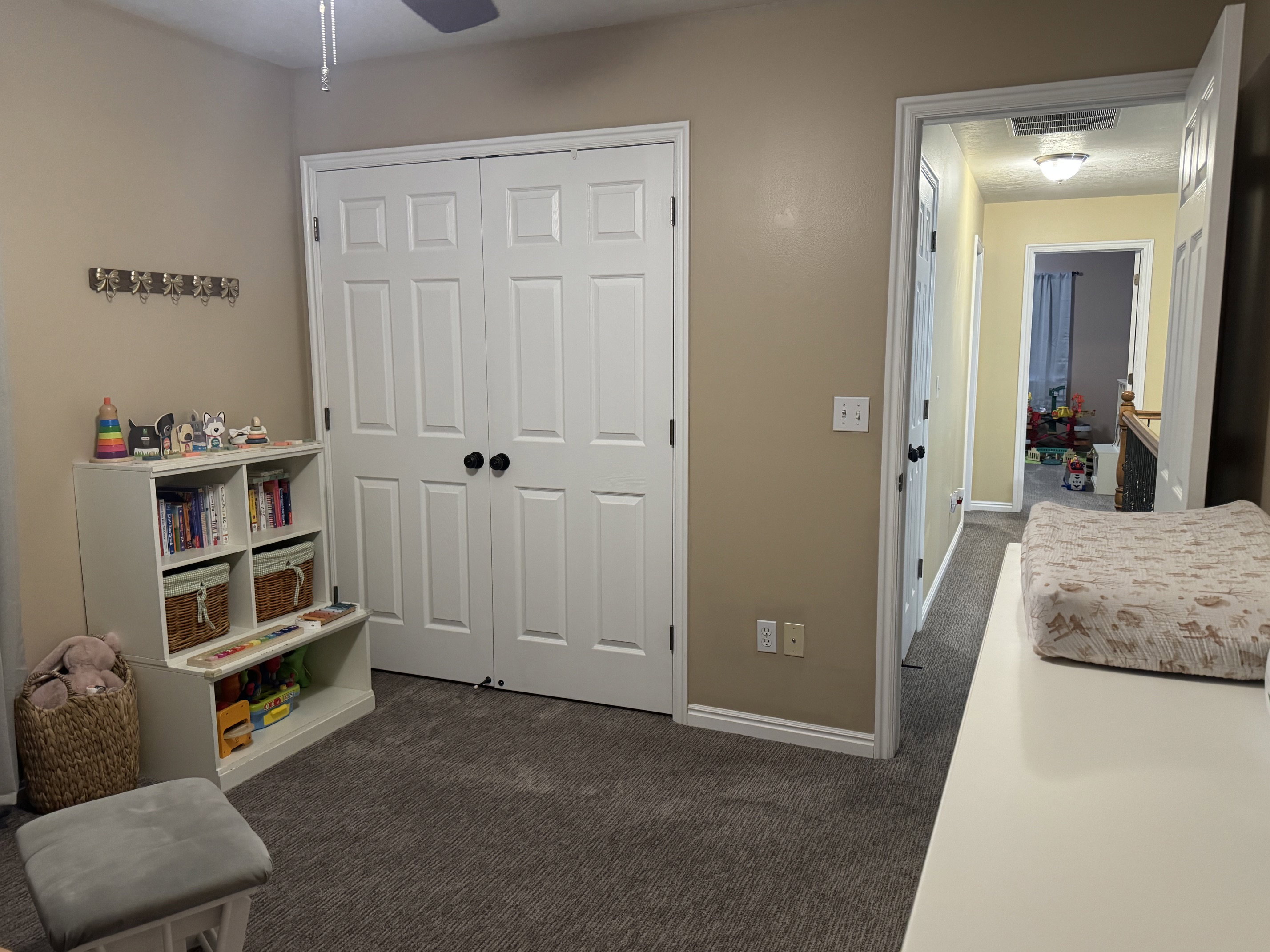 Neutral-toned room featuring a ceiling fan, plush carpet flooring, bi-fold closet doors with black hardware, and white trim