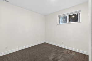 Spare room featuring dark colored carpet and baseboards