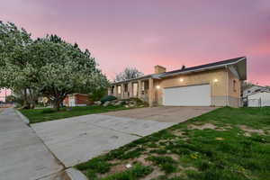Single story home featuring brick siding, concrete driveway, an attached garage, a chimney, and a yard