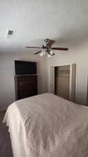 Bedroom with a closet, ceiling fan, a textured ceiling, and dark colored carpet