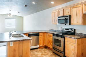 Kitchen featuring stainless steel appliances, a peninsula, dark countertops, and a ceiling fan