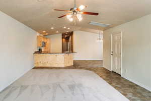 Unfurnished living room with ceiling fan, dark colored carpet, hanging lights, stone finish floors, and vaulted ceiling