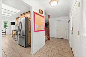 Kitchen featuring a textured ceiling, light tile patterned floors, stainless steel appliances, ornamental molding, and wood finish cabinetry