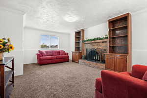 Living area featuring ornamental molding, carpet floors, a brick fireplace, and a textured ceiling