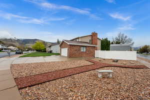View of property exterior featuring driveway, a garage, a mountain view, a chimney, and brick siding