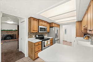 Kitchen with light countertops, stainless steel appliances, wood finish cabinets, light carpet, and light tile patterned floors