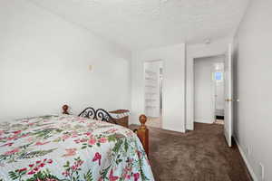 Bedroom with a spacious closet, dark colored carpet, and a textured ceiling
