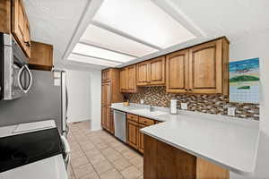 Kitchen featuring wood finish cabinets, stainless steel appliances, a textured ceiling, light tile patterned floors, and a peninsula