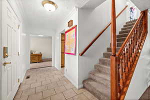 Stairs featuring a textured ceiling, carpet floors, crown molding, and tile patterned floors