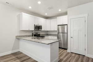Kitchen with light stone countertops, stainless steel appliances, a peninsula, white cabinets, and light wood-style floors