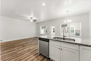 Kitchen featuring dishwasher, white cabinetry, dark wood-type flooring, suspended lighting, and light stone countertops