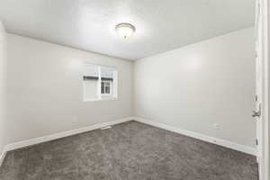 Spare room featuring dark carpet and a textured ceiling