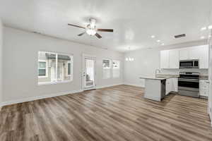 Kitchen with open floor plan, stainless steel appliances, suspended lighting, white cabinetry, and a peninsula
