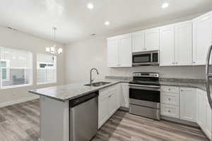 Kitchen featuring stainless steel appliances, light stone countertops, white cabinets, a peninsula, and light wood-type flooring