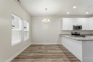 Kitchen featuring light stone countertops, light wood finished floors, white cabinetry, hanging lights, and a textured ceiling