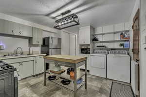Kitchen with light countertops, black appliances, a textured ceiling, stone finish floors, and separate washer and dryer