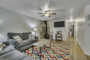 Living room featuring a wood stove, light wood-style flooring, and a ceiling fan