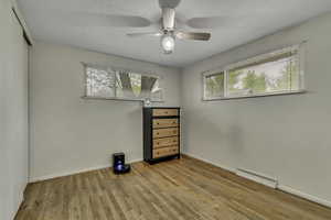 Unfurnished bedroom with light wood finished floors, a ceiling fan, and a baseboard radiator