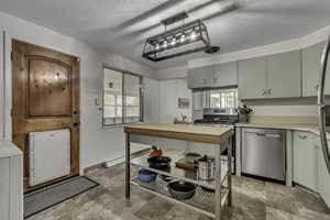Kitchen featuring light countertops, stainless steel appliances, stone finish floors, a textured ceiling, and washer / clothes dryer
