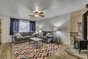 Living area with a wood stove, light wood-style floors, a textured ceiling, a ceiling fan, and wood walls