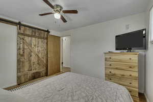 Bedroom featuring wood finished floors, ceiling fan, and a barn door