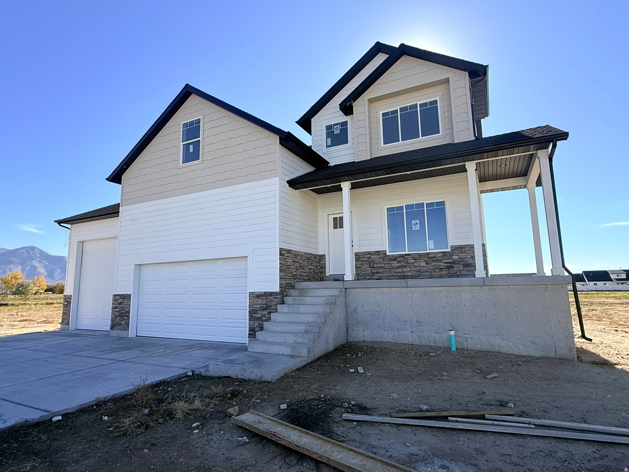 View of front of property featuring concrete driveway, stone siding, covered porch, a garage, and a mountain view