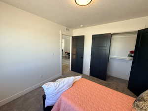 Bedroom with a closet, dark colored carpet, and a textured ceiling