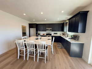 Kitchen featuring a center island, stainless steel appliances, light wood-style floors, a breakfast bar, and light stone countertops