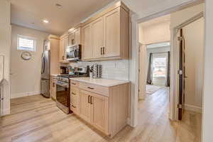 Kitchen with light wood finish cabinets, stainless steel appliances, light wood-style flooring, tasteful backsplash, and recessed lighting