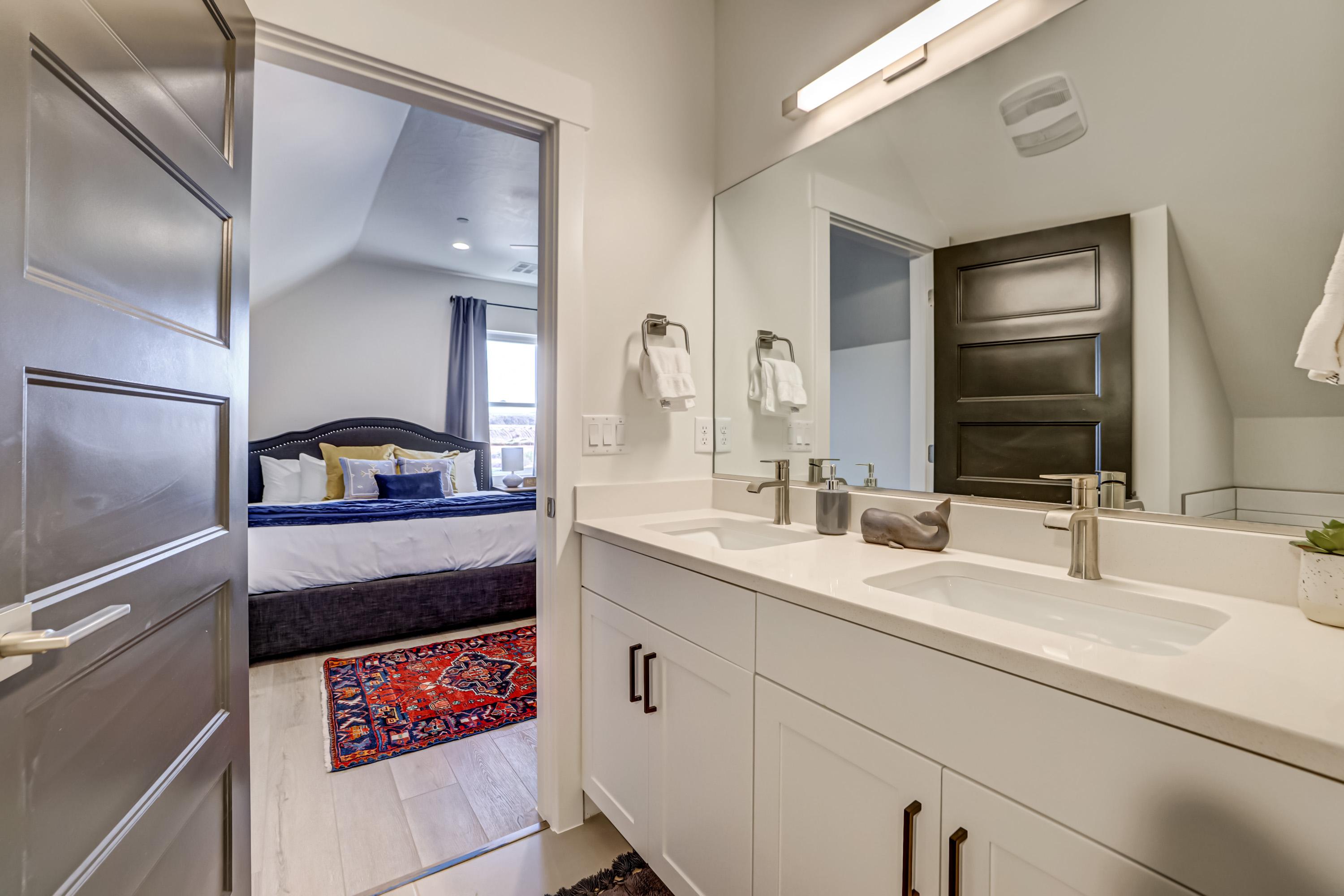 Ensuite bathroom featuring double vanity, vaulted ceiling, and light wood-style flooring