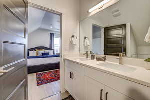 Ensuite bathroom featuring double vanity, vaulted ceiling, and light wood-style flooring