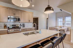 Kitchen with light wood finish cabinets, stainless steel appliances, decorative backsplash, a kitchen breakfast bar, and light wood-style flooring