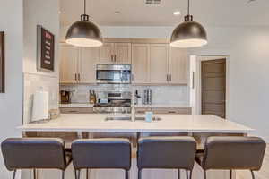 Kitchen with light wood finish cabinets, a breakfast bar, stainless steel appliances, and light stone counters