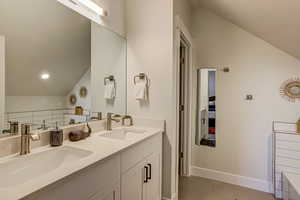 Full bath with vaulted ceiling, double vanity, and light tile patterned floors