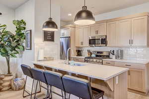Kitchen with a kitchen bar, a peninsula, stainless steel appliances, light wood finish cabinetry, and light stone countertops