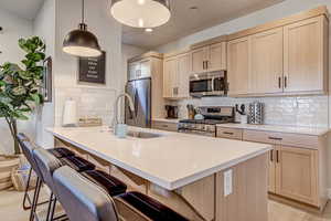Kitchen featuring light wood finish cabinets, a peninsula, stainless steel appliances, a kitchen breakfast bar, and light stone countertops